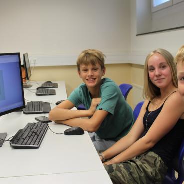 Jugendliche in einem Computerraum in Österreich sitzen lächelnd vor Bildschirmen.